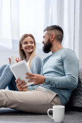 Couple smiling and sitting in casual clothing with digital tablet