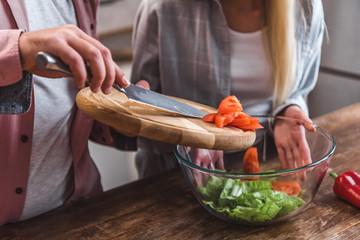 Cropped view of man adding tomatoes in salad and woman holding bowl