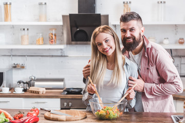 smiling couple hugging while cooking dinner at kitchen