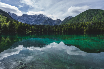View of a mountain lake Lago Fusine, Julian alps and Tirol. Beautiful and clear alpine lake with blue and green colors, deep forest and high alpine peaks and rock faces.