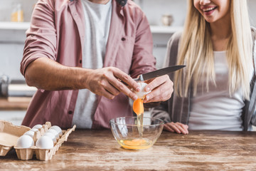 cropped view of man smashing eggs in bowl at kitchen table