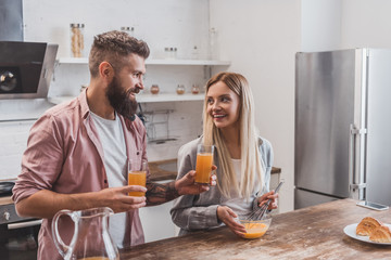 young smiling woman preparing breakfast while handsome man holding glasses with juice