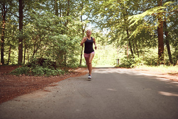 Fit young blonde woman running alone on a forest path