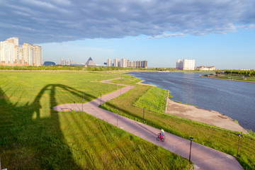 father and daughter riding bikes along the river towards city taken from bridge
