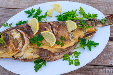 Baked carp fish with lemon and parsley on wooden table