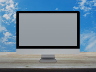 Desktop modern computer monitor with grey wide screen on wooden table over blue sky with white clouds