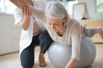 Senior woman exercising with her physiotherapist and swiss ball - obrazy, fototapety, plakaty
