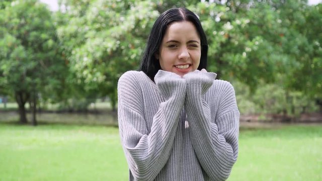 Young attractive woman freezing and shivering in gray sweater in the park