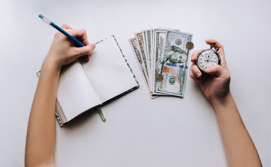 Dollars, notebook, pen. Woman's hand holding a grey stopwatch over white background. Usurer, credit concept. Time for quick money.