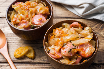 Stewed cabbage with sausages in wooden bowls on the table. Selective focus.
