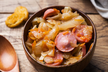Stewed cabbage with sausages in wooden bowls on the table. Selective focus.