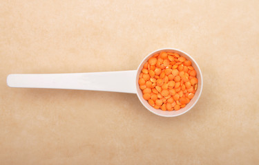 Rote Linsen auf Dosierlöffel und braunem Hintergrund