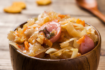 Stewed cabbage with sausages in wooden bowls on the table. Selective focus.