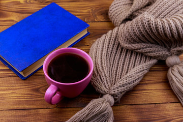 Cup of coffee, knitted scarf and book on wooden background