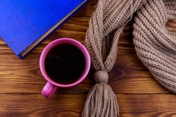 Cup of coffee, knitted scarf and book on wooden background