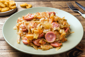 Stewed cabbage with sausages in a plate on the table. Selective focus.
