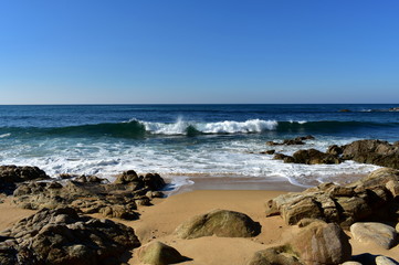 Fototapeta na wymiar Wild beach with rocks, golden sand and waves with foam. Sunny day, blue sky. Galicia, Spain.