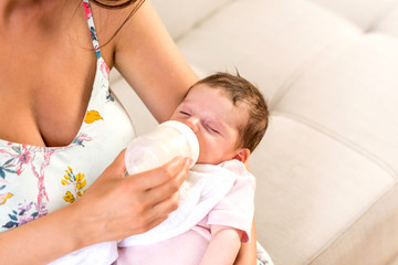 Closeup photo of a baby while her mother feeding her on a sofa in the living room.