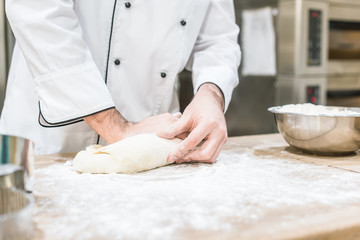 close up of baker hands with uncooked dough on cutting board