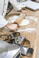 close up of baker hands rolling out uncooked dough on wooden table