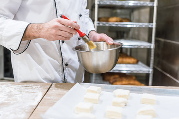 close up of baker hands oiling dough pieces with basting brush