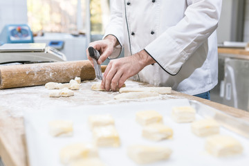 Cropped view of baker hands cutting dough on table