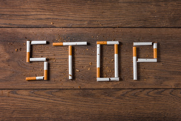Creative background, the word stop is made up of cigarettes on a brown wooden background. The concept of smoking kills nicotine poisons. Copy space.