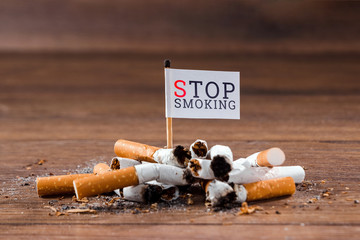 Creative background. A pile of cigarette butts on a wooden background, the inscription stop smoking. The concept of smoking kills, nicatine poisons, cancer from smoking, stop smoking. Copy space.