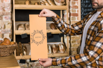 male seller holding paper menu in hands at bakery