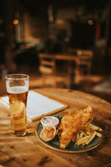 Fish and chips plate and pint of beer on a wooden table at the pub. - 235649756