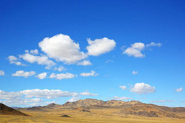 Fototapeta na wymiar The rural road in the desert behind the mountain range with sky blue and cluods. Central Asia between the Russian Altai and Western Mongolia 