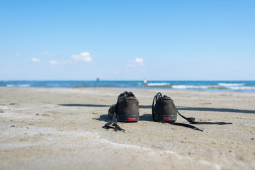 Black sneakers on the sand on the sea background. Summer and travel concept