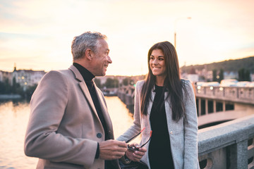 Man and woman business partners standing by a river in city at dusk, talking.