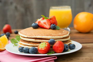 Homemade american pancake with fresh blueberries, strawberries and orange juice. Wooden rustic background.
