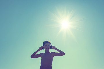 Silhouette of teen boy on the beach in the headphones opposite sun. Traveling on an airplane with children.Concept