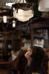 Obraz na płótnie Canvas Young girl looking at a retro lamp in an antique shop
