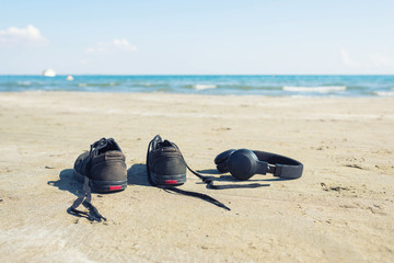 Black sneakers with headphones on the sand on the sea background. Summer and travel concept 
