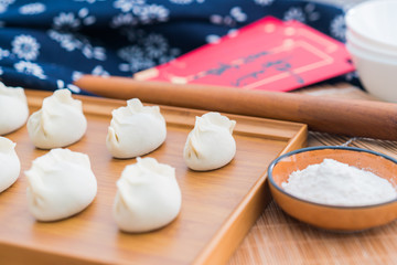 Dumplings, flour, rolling sticks, red envelopes on the wooden table
