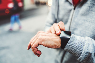 A close-up of unrecognizable man standing outdoors in city, using smartwatch.