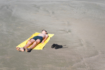 Top view on  the teen boy lies on yellow towel and sunbathes on the beach on the sea and sky background. Concept