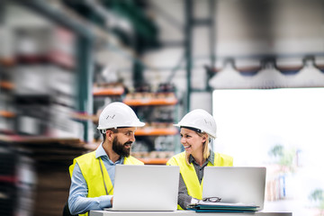 A portrait of an industrial man and woman engineer with laptop in a factory, working.