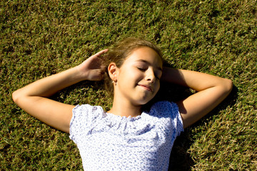 A young girl lies on the mown grass stretching her arms