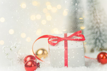 Small elegant silver gift box tied with red silk ribbon in winter scene in forest with fir trees snow ornaments. Christmas New Years presents holiday magic atmosphere. Greeting card banner poster