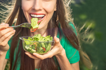 Beautiful caucasian woman eating salad over green natural background	 - Powered by Adobe