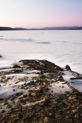A beautiful view from the coast to the freezing lake against the backdrop of a gloomy sky with sunset. Winter snow covered lake Turgoyak. Landscape.