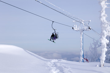 Fototapeta na wymiar Russia, Sheregesh 2018.11.17 Snowboarder and skier in professional outfit climb up cable car lift up mountains on background of sky and mountain peaks. Concept safety skiing, outdoor rest, friendship