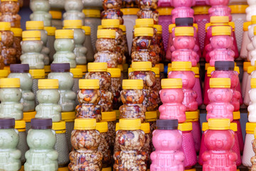 Many transparent plastic jars with yellow lids in the shape of a bear with green, pink honey mixed with nuts. Concept of local Siberian delicacies and specialties