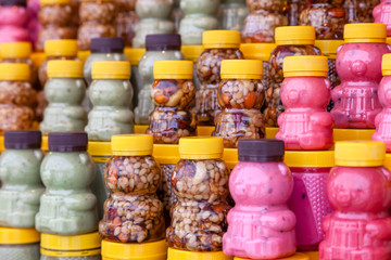 Fototapeta premium Many transparent plastic jars with yellow lids in the shape of a bear with green, pink honey mixed with nuts. Concept of local Siberian delicacies and specialties