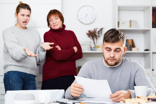 Distressed man with paperwork with irritated family behind
