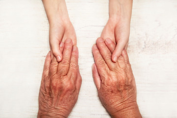 hands of an elderly woman holding young hands, parting words, symbol, on a light background, close-up